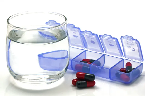 Orale Medikamente rote und schwarze Kapseln in separater Dosisbox auf weißem Hintergrund. lizenzfreie Stockfotos