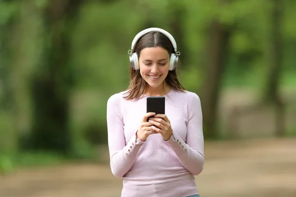 フロントビューポートレート公園内の電話で音楽を聞いて歩く無線ヘッドフォンを身に着けている幸せな女性 — ストック写真