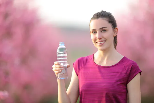 Deportiva Feliz Sosteniendo Botella Agua Mirándote Pie Campo Rosa Florecido — Foto de Stock