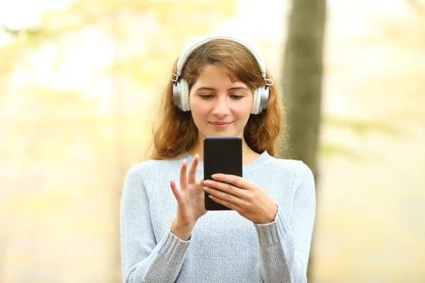 公園でヘッドフォンや携帯電話を身に着けている音楽を聞いている女性のフロントビューの肖像画 — ストック写真