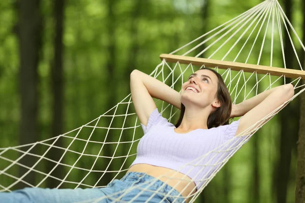 幸せな女性はハンモックに横たわって緑の森の中で休日を見上げ — ストック写真