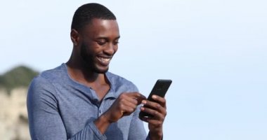 Açık havada akıllı telefon kullanan siyah tenli mutlu bir adam.