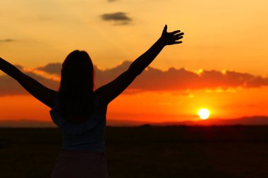 Back view of a silhouette of a woman outstretching arms at sunset