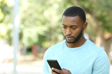 Siyah tenli endişeli adam parkta cep telefonunu kontrol ediyor.