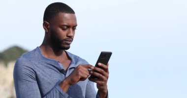 Siyah tenli bir adam güneşli bir günde dağda akıllı telefon kullanıyor.