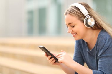 Kulaklık takıp müzik dinleyen mutlu gençler kampüste akıllı telefonları kontrol ediyorlar.