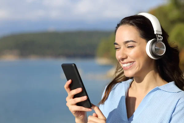 快乐的女人 戴着无线耳机 在湖中听音乐 检查智能手机 — 图库照片
