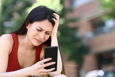 Endişeli Asyalı kadın sokakta akıllı telefonu kontrol ediyor.