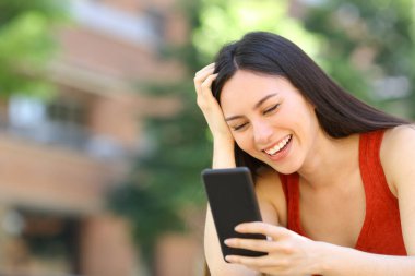 Mutlu Asyalı kadın sokakta akıllı telefon mesajlarını kontrol ediyor.