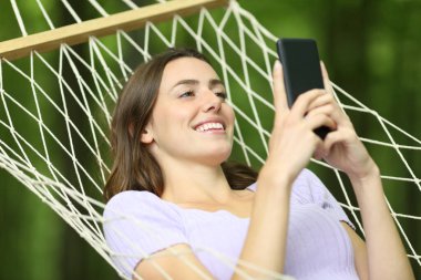 Mutlu kadın, tatilde hamakta uzanan akıllı telefonu kullanıyor.