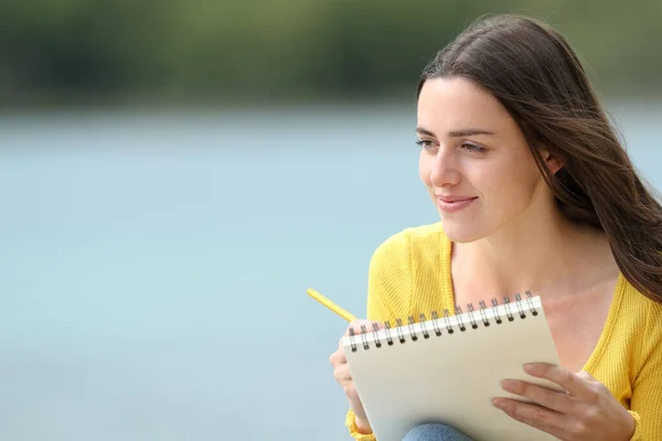 Satisfied woman drawing on notebook sitting in a lake