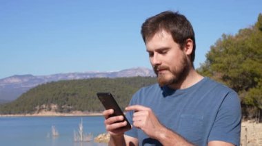 Şaşkın yakışıklı adam dışarıda telefon haberlerini kontrol ediyor.