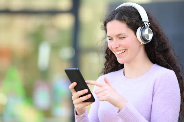 路上でヘッドフォンを身に着けている音楽を聞いて幸せな女性はスマートフォンをチェック — ストック写真