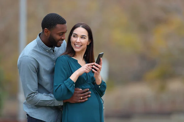 Interracial Couple Enjoying Pregnancy Holding Cell Phone Park — Stock Photo, Image