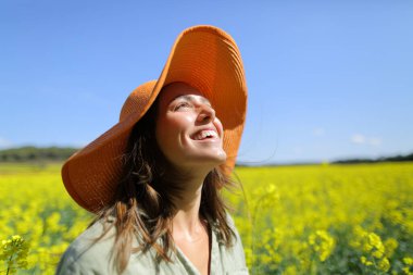 Turuncu pamela şapkalı mutlu kadın güneşli bir günde yukarıdaki tarlaya bakıp gülüyor.