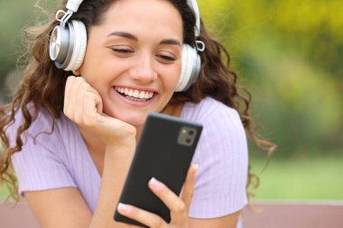 Bir bankta oturup telefonla video izleyen mutlu bir kadının portresi.