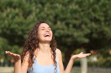 Güneşli bir günde aniden yağan yağmurun altında gülen ve eğlenen mutlu bir kadın.