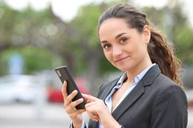 Akıllı telefonu tutan ve sokaktaki kameraya bakan kendine güvenen bir yönetici.