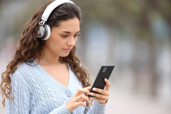 一个严肃的女人 带着无线耳机 在街上听着音乐 听着智能手机 — 图库照片