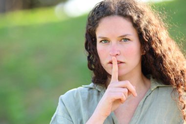 Ciddi bir kadın parkta parmakları dudaklarında sessizlik istiyor.