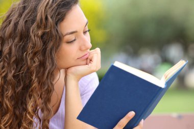 Parkta yalnız başına kitap okuyan rahat bir kadın.