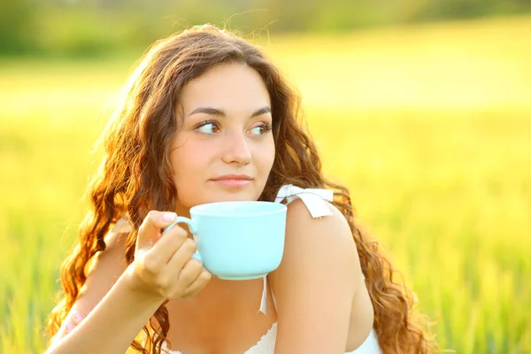 Pensive woman drinking coffee and looking at side in a wheat field at sunset