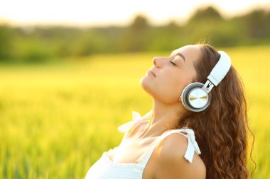 Meditasyon yapan, buğday tarlasında kulaklıkla müzik dinleyen bir kadının yan görüntüsü.