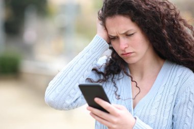 Worried woman checks smart phone content standing in the street