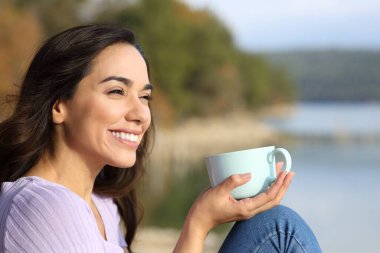 Happy woman drinking coffee contemplating views and enjoying peace in a lake on vacation