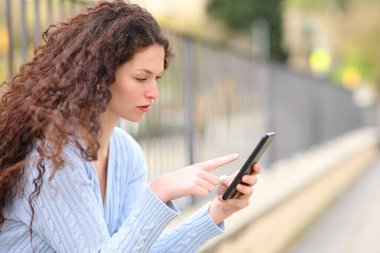 Side view of a serious woman using cell phone sitting in the street