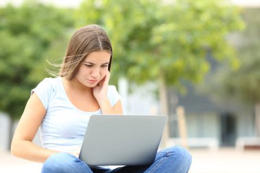 Concentrated teen using laptop sitting in the street