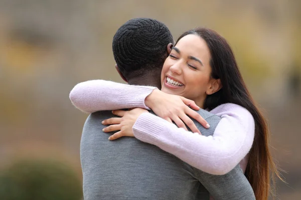 Happy woman meeting and hugging a man with black skin in a park