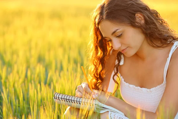 Woman drawing or writing in a notebook in a wheat field