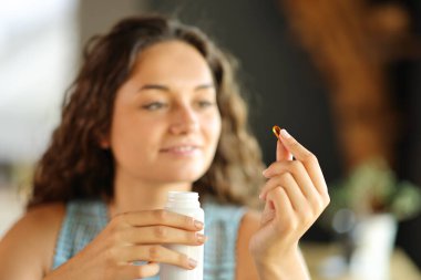 Happy woman holding a vitamin pill sitting in a restaurant