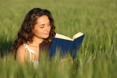 Woman reading a paper book sitting in a green wheat field