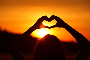 Gün batımında ya da gündoğumunda kalp şekli yapan kadın ellerinin yakın portresi