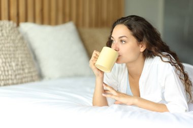 Yatak odasındaki yatakta kahve içen bir kadın.
