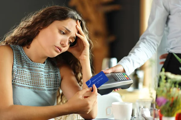 Worried customer paying expensive bill with credit card in a restaurant