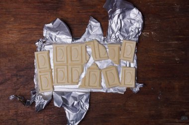 Kırık beyaz çubuk ya da kahverengi ahşap arka planda folyo üzerine hindistan cevizi çikolatası. Eşsiz tatlılar, alışılmadık çikolata aromalı.