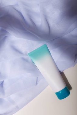 Mavi şapkalı beyaz model tüp, beyaz kumaşta etiket yok, doğal katı gölgeler var. Şablon, uzayı kopyala. Yüz bakımı kozmetikleri, krem
