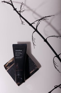 İzmail, Ukrayna, Temmuz 2021. Yüz için siyah tüp kil maske, cilt bakım kozmetikleri, güvertede koyu ışıkta dallı, gölgeli beyaz