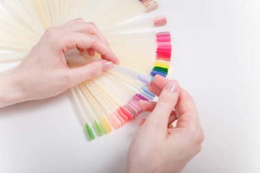 Manikür için manikür rengini palet renklerinden seçen bir müşteri. Yaklaş, sadece ellerini beyaz masaya koy. Tırnak sanatı, el bakımı, güzellik konsepti.