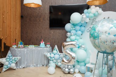 Oğlanın doğum günü partisi için mavi balon kemeri. 5 numara ve 2 kardeş için 1 numara. Dekoratif unsurlar, yıldızlı fotoğraf bölgesi, iki pasta ve şekerli gofret.. 