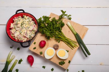 Turp, yeşil soğan, maydanoz, kırmızı kasede yumurta salatası beyaz ahşap arka planda mutfak tahtası. Sağlıklı yeme alışkanlıkları, organik gıda, diyet ve beslenme konsepti.