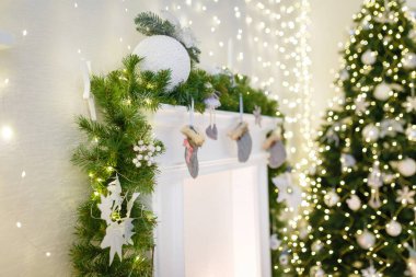 Noel arifesinde dekoratif detaylar. Köknar dallı şömine, beyaz mücevherli Noel ağacı ve parlak çelenk.
