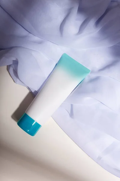 White mockup tube with blue cap, no label on white fabric, with natural solid shadows. Template, copy space. Face skin care cosmetics, creme