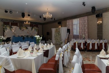 Düğün için dekore edilmiş restoran, damat ve gelin için başkanlık, konuklar için masalar, çiçekli fotoğraf bölgesi ve mumlar..