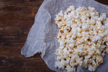 Beyaz kağıt üzerinde tuzlanmış patlamış mısır yığını. Kahverengi masa arkası, yakın çekim.