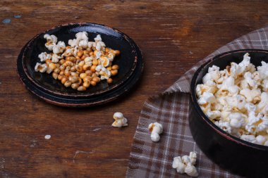 Tahta kırsal arka planda siyah kasede hazır ve çiğ patlamış mısır yığını. Kumaş ve masada patlamış mısır.
