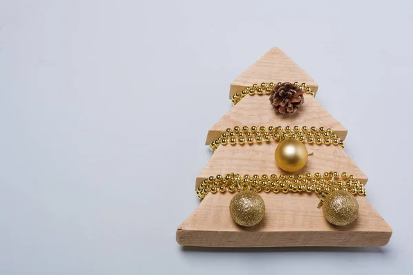 从木板上剪下的木制冷杉玩具 装饰着金色的珠子和灌木 在轻盈的背景上装饰着灯泡 圣诞快乐 新年快乐 — 图库照片
